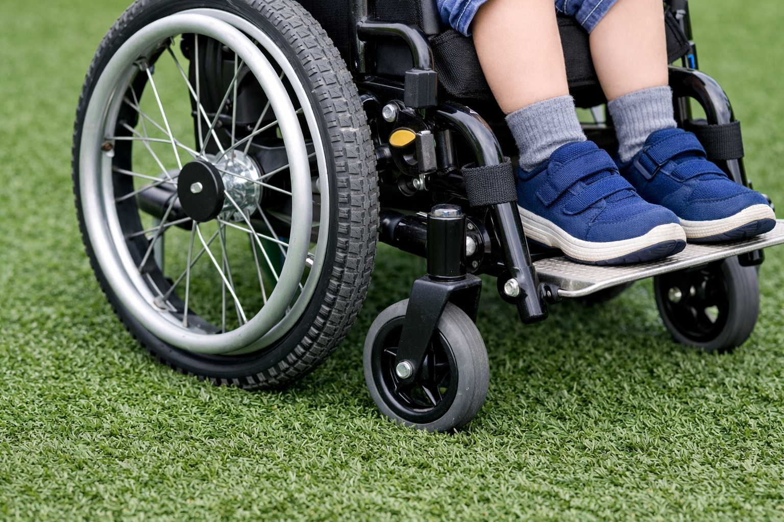 Child in Wheelchair on Synthetic Turf Zoomed In on Wheels